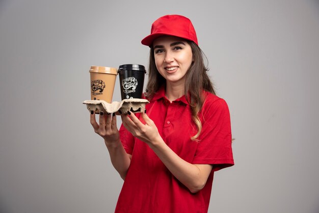 コーヒーカップを保持している赤い制服を着た美しい配達の女性。