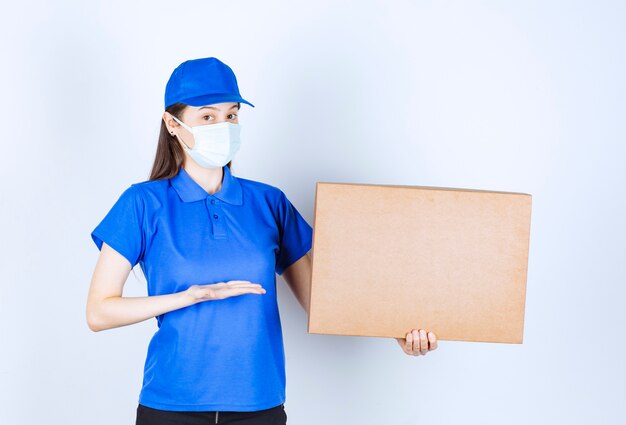 Красивая доставщица в медицинской маске, держащей картонную упаковку.