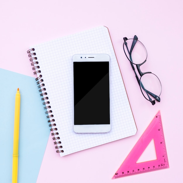 Beautiful desktop composition with phone, notebook, glasses on pink background