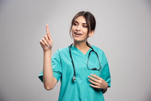 Beautiful doctor pointing at something on gray