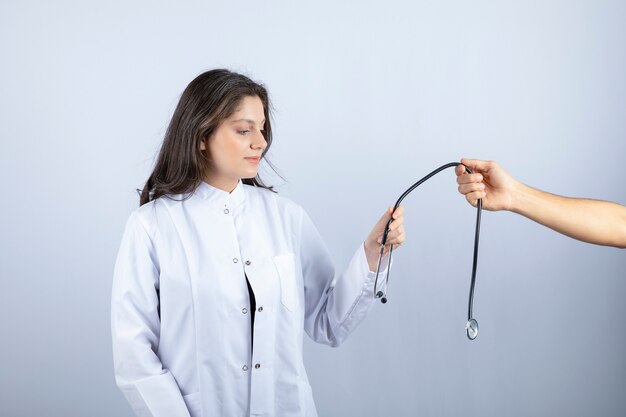 Beautiful doctor in white coat taking stethoscope from another person. 