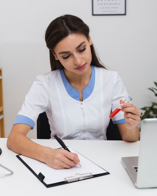 Beautiful doctor writing a report and holding a blood sample