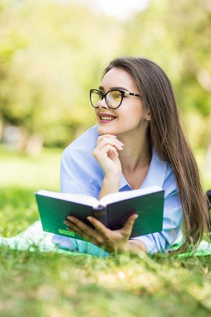 Beautiful dreamy teen girl lying on grass in citypark with pen and notebook