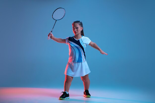 Beautiful dwarf woman practicing in badminton isolated on blue in neon light