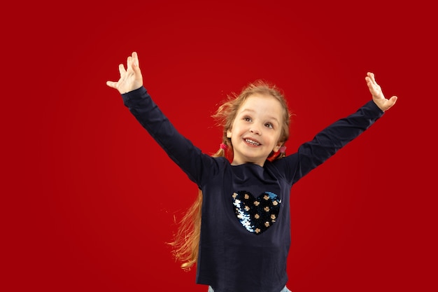 Beautiful emotional little girl isolated on red studio