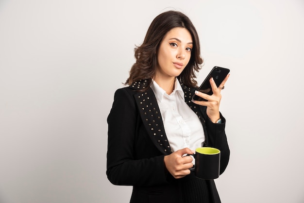 Bella dipendente che tiene tazza di tè e telefono