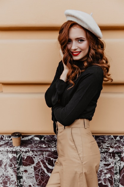 良い一日を楽しんでいる茶色のベレー帽の美しいヨーロッパの女性。屋外でポーズをとる生姜髪の素晴らしいフランスの女性モデル。