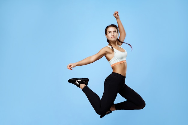 Бесплатное фото Красивая, возбужденная фитнес женщина в красочной спортивной одежде, прыгает высоко