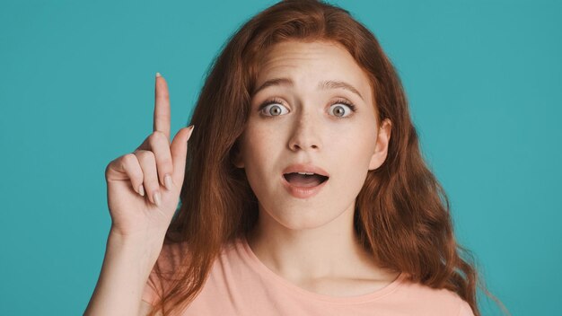 Beautiful excited redhead girl showing new idea gesture amazedly looking in camera over colorful background Wow expression