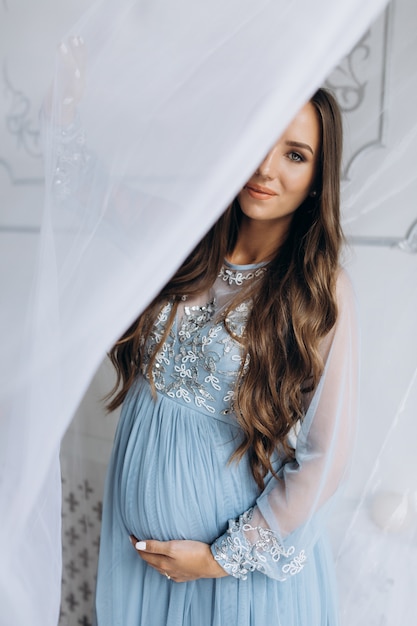  Beautiful expecting woman in blue dress poses in a studio