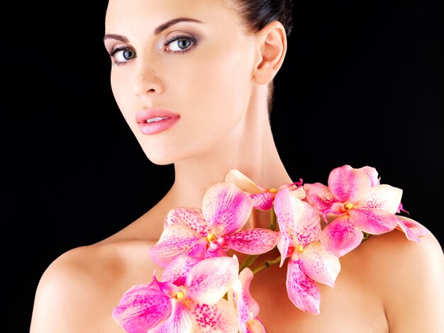 Beautiful face of an adult woman with healthy skin and pink flowers on body - studio