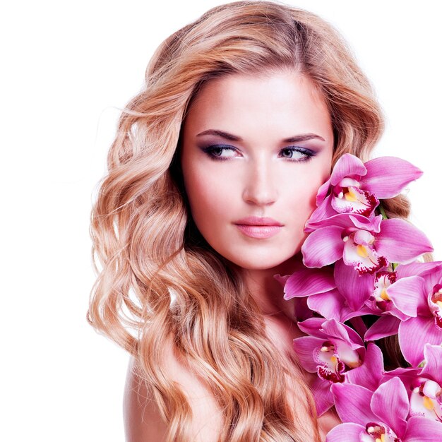Красивое лицо молодой блондинки со здоровыми волосами и розовыми цветами возле лица - изолированного на белом.