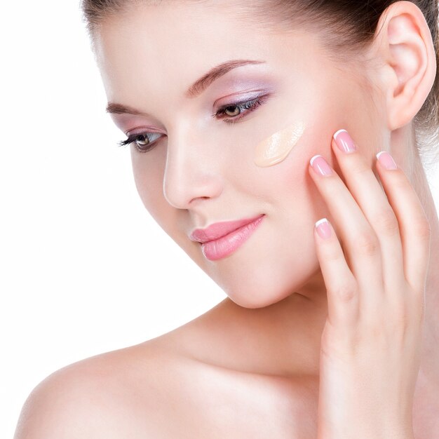 Beautiful face of young woman with cosmetic foundation on a skin over white wall. Beauty treatment concept.