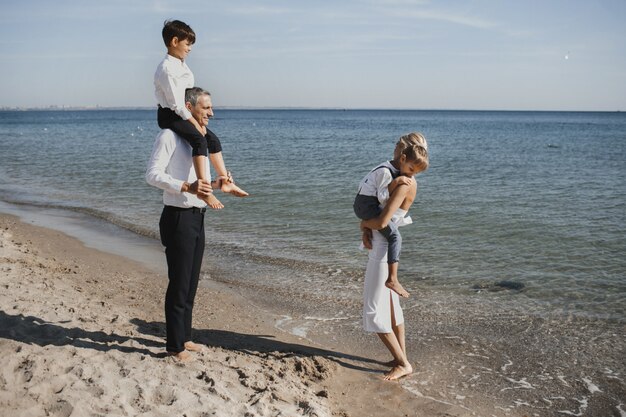 美しい家族は、晴れた夏の日に、海岸線、両親と2人の息子を歩いています。