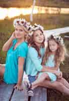 Free photo beautiful family. mother and her daughters relaxing outdoors while sitting on a wooden path in a field at sunset.
