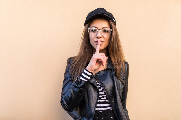 Beautiful fashion girl in leather jacket and black hat isolated on light yellow wall