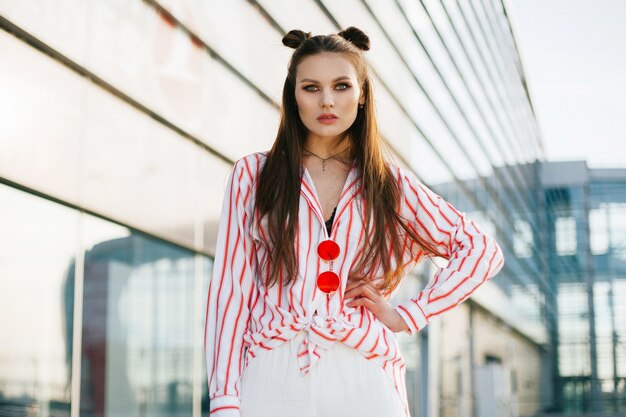 Beautiful fashion model with long hair poses before modern glass building outside