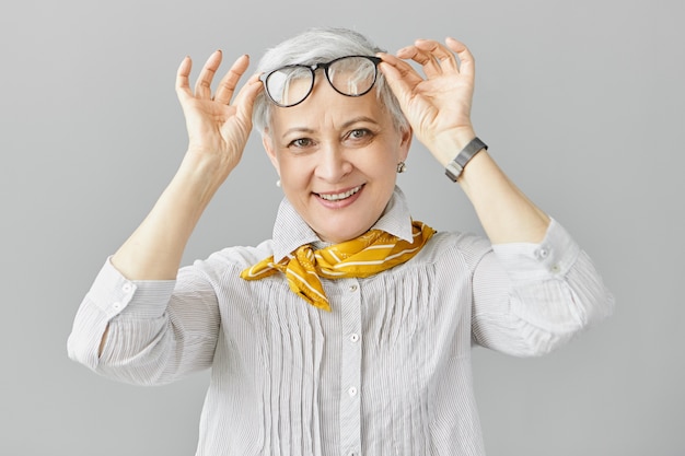 Бесплатное фото Красивая модная женщина-пенсионерка кавказской с дальнозоркостью, снимая очки, чтобы сосредоточиться на более близких объектах, широко улыбаясь. зрелые люди, старение и концепция проблемы зрения
