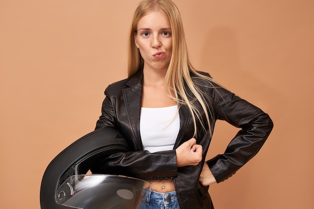 Beautiful fashionable young blonde female biker wearing stylish black leather jacket having confident facial expression