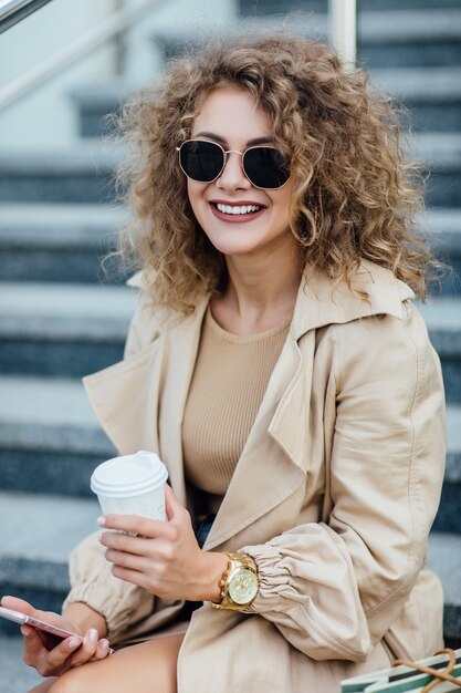 Free photo beautiful and fashionable young woman with shopping bags siting on city street and looking over shoulder.