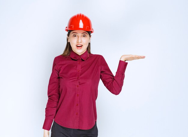 Beautiful female architect in red helmet standing and holding open space. 