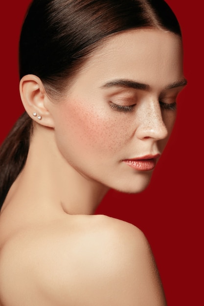 A beautiful female face. Perfect and clean skin of young caucasian woman on red studio background.