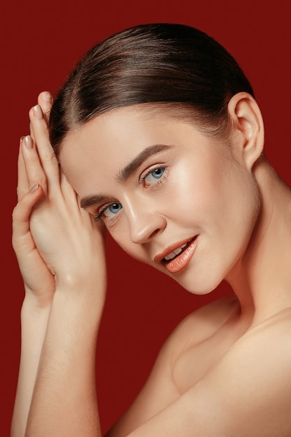 Free photo a beautiful female face. perfect and clean skin of young caucasian woman on red studio background.