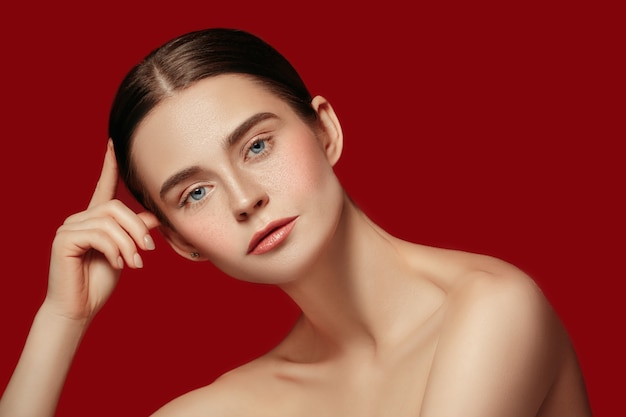 A beautiful female face. Perfect and clean skin of young caucasian woman on red studio background.