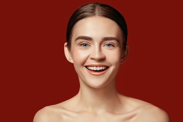 美しい女性の顔。赤いスタジオの背景に若い白人女性の完璧できれいな肌。