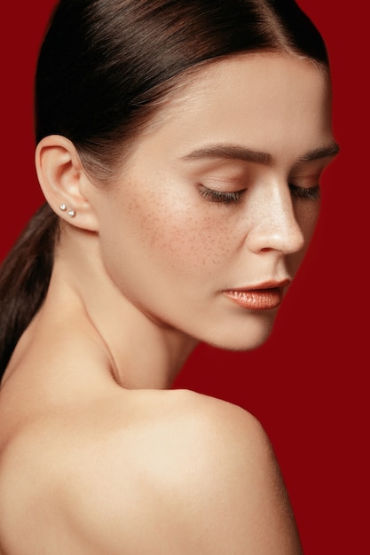 A beautiful female face. Perfect and clean skin of young caucasian woman on red studio.