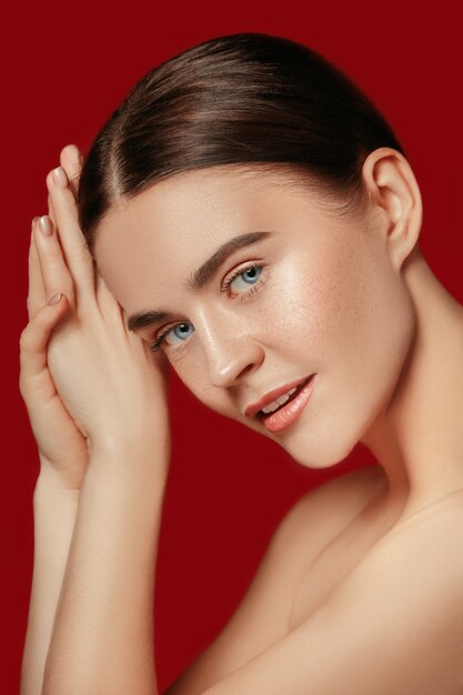 A beautiful female face. Perfect and clean skin of young caucasian woman on red studio.