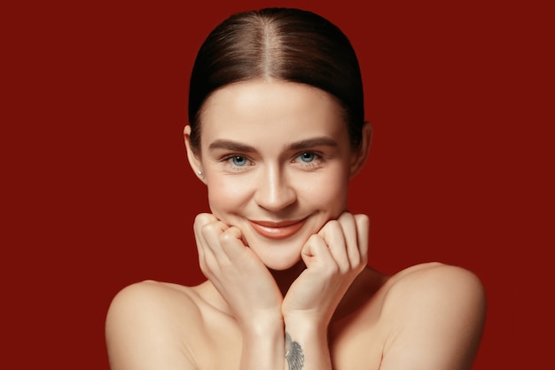 A beautiful female face. Perfect and clean skin of young caucasian woman on red studio.