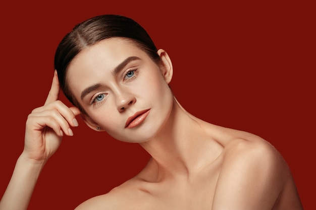 美しい女性の顔。赤いスタジオの若い白人女性の完璧できれいな肌。