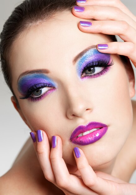 Beautiful  female face with fashion  make-up of eyes and beauty purple manicure. She put her hands on face.