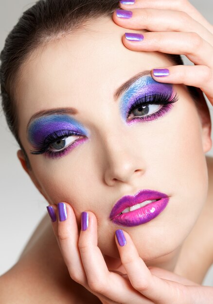 Красивое женское лицо с модным макияжем глаз и фиолетовым маникюром красоты. Она положила руки на лицо.