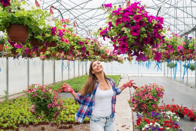 Красивая женщина-флорист держит горшечные цветочные растения в теплице, чувствуя себя счастливой и позитивной