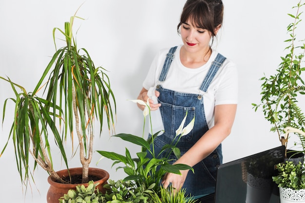 Beautiful female florist spraying water on potted plants in floral shop