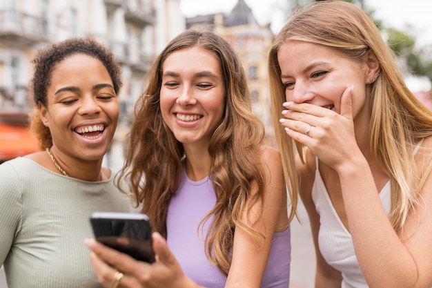 Free photo beautiful female friends smiling at the mobile phone