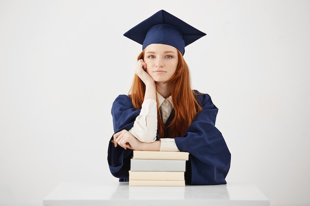 Beautiful female graduate sitting with books smiling. 