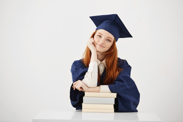 Beautiful female graduate sitting with books smiling.