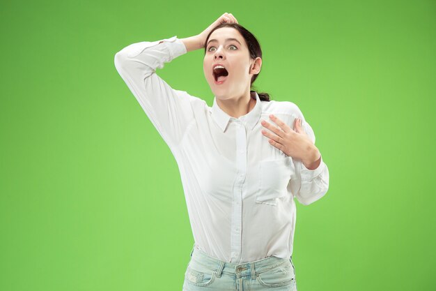 Beautiful female half-length front portrait isolated on green studio background. Young emotional surprised woman standing with open mouth.