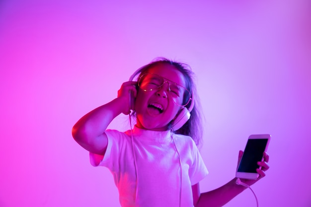 Beautiful female half-length portrait isolated on purple backgroud in neon light. Emotional girl in eyeglasses. Human emotions, facial expression concept. Dancing, listening to music, making selfie.