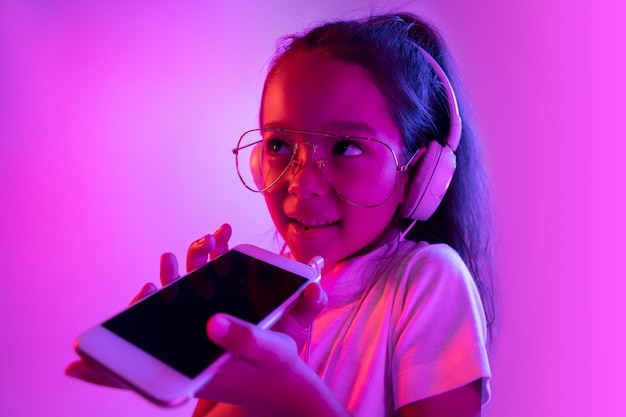 Free photo beautiful female half-length portrait isolated on purple backgroud in neon light. emotional girl in eyeglasses. human emotions, facial expression concept. listening to music, recording voice message.