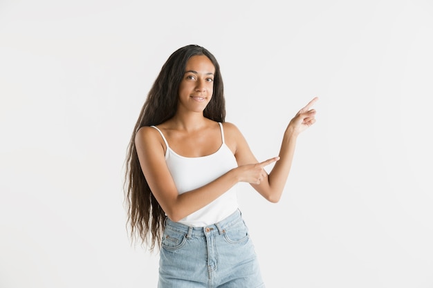 Beautiful female half-length portrait isolated on white studio background. Young emotional african-american woman with long hair. Facial expression, human emotions concept. Showing an empty space bar.