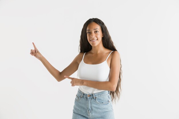 Beautiful female half-length portrait isolated on white studio background. Young emotional african-american woman with long hair. Facial expression, human emotions concept. Showing an empty space bar.