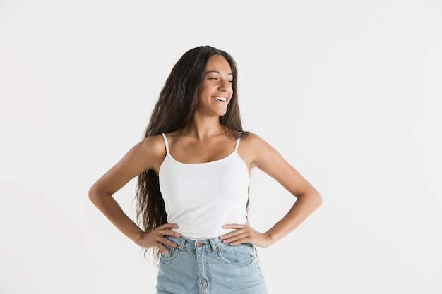 Beautiful female half-length portrait isolated on white studio background. Young emotional african-american woman with long hair. Facial expression, human emotions concept. Standing and smiling.