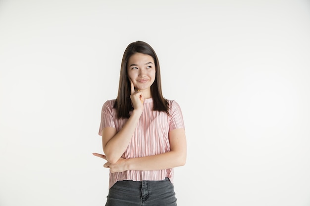 Beautiful female half-length portrait isolated on white studio background. Young emotional woman in casual clothes. Human emotions, facial expression concept. Thinks or dreams, looks thoughtful.