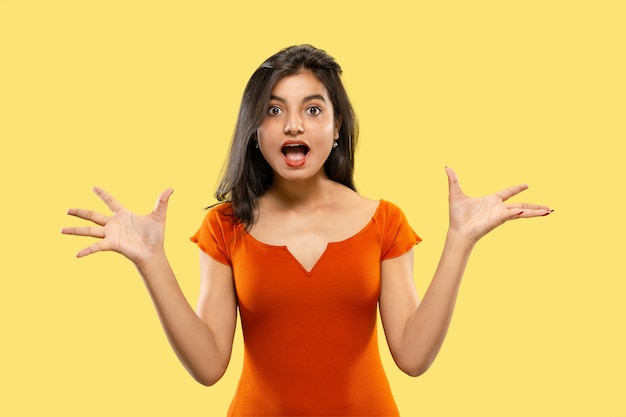 Beautiful female half-length portrait isolated on yellow  space. Young emotional indian woman in dress astonished and happy. Negative space