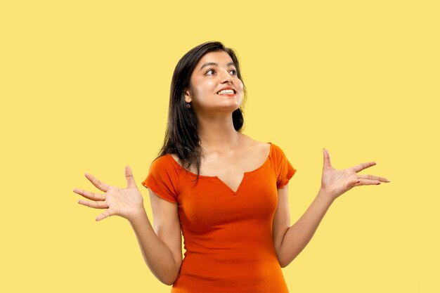 Beautiful female half-length portrait isolated on yellow  space. Young emotional indian woman in dress astonished and happy. Negative space