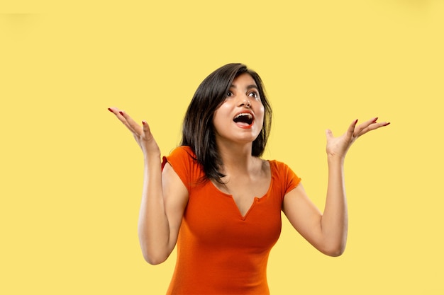 Beautiful female half-length portrait isolated on yellow  space. Young emotional indian woman in dress astonished and happy. Negative space